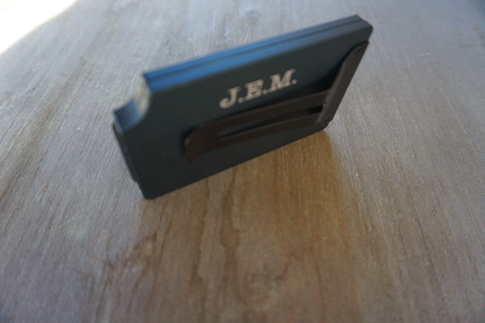 Black rectangular object with 'J.E.M.' branding on a wooden surface