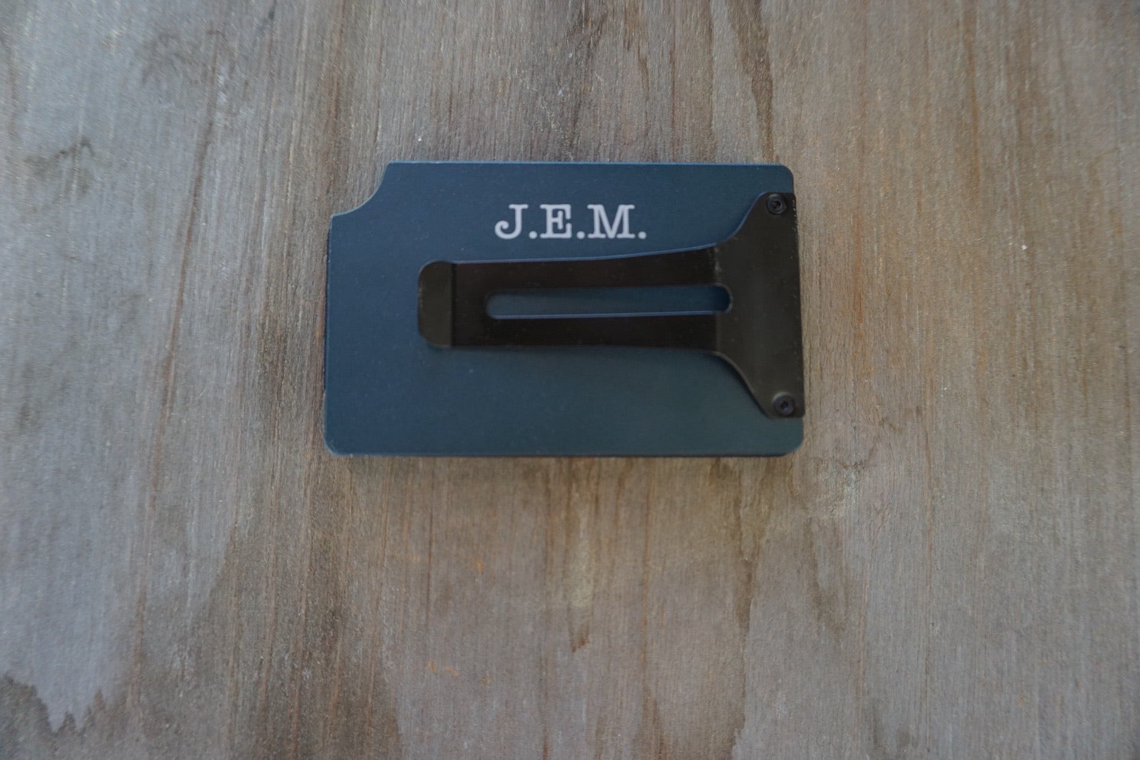 Black metal bracket with 'J.E.M.' engraving on a wooden surface