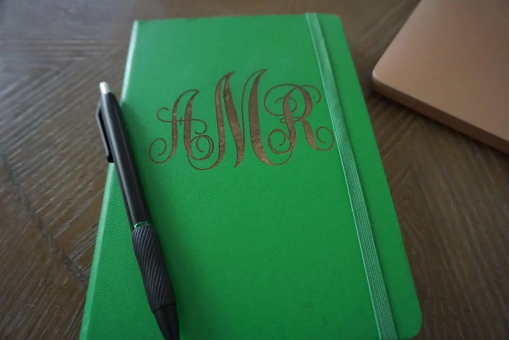 Green notebook with 'MNR' monogram and a pen on a wooden surface