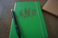 Green notebook with 'MNR' monogram and a pen on a wooden surface