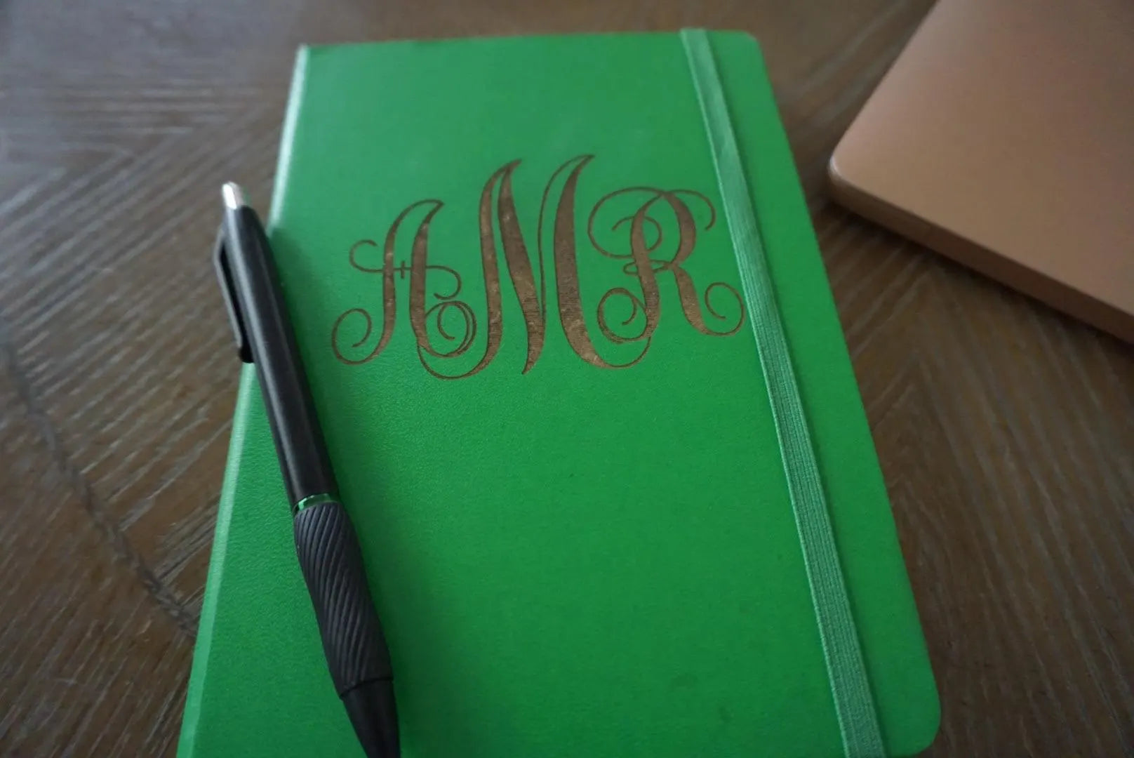 Green notebook with 'MNR' monogram and a pen on a wooden surface