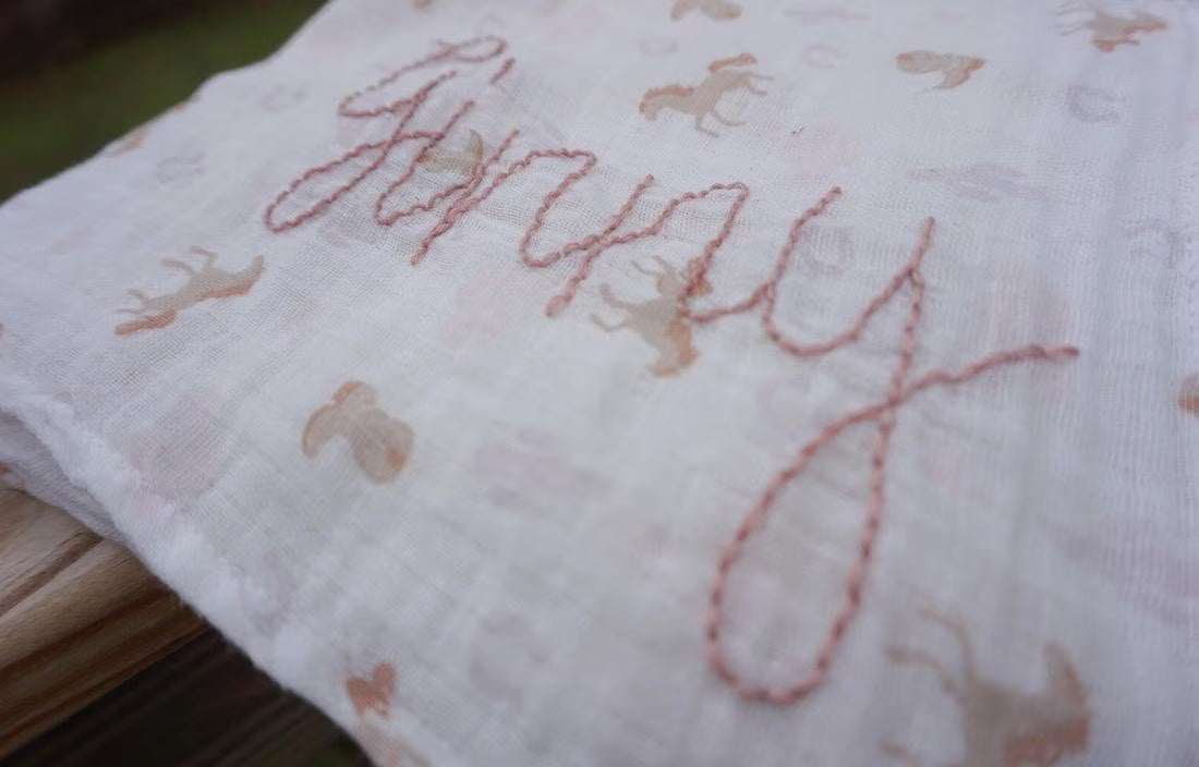 Embroidered fabric with 'Happy' text and animal patterns on a wooden surface