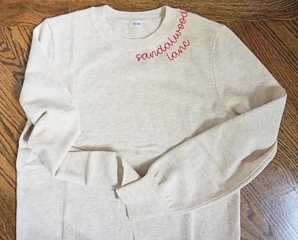 Beige sweatshirt with 'sandalwood lane' text on a wooden surface