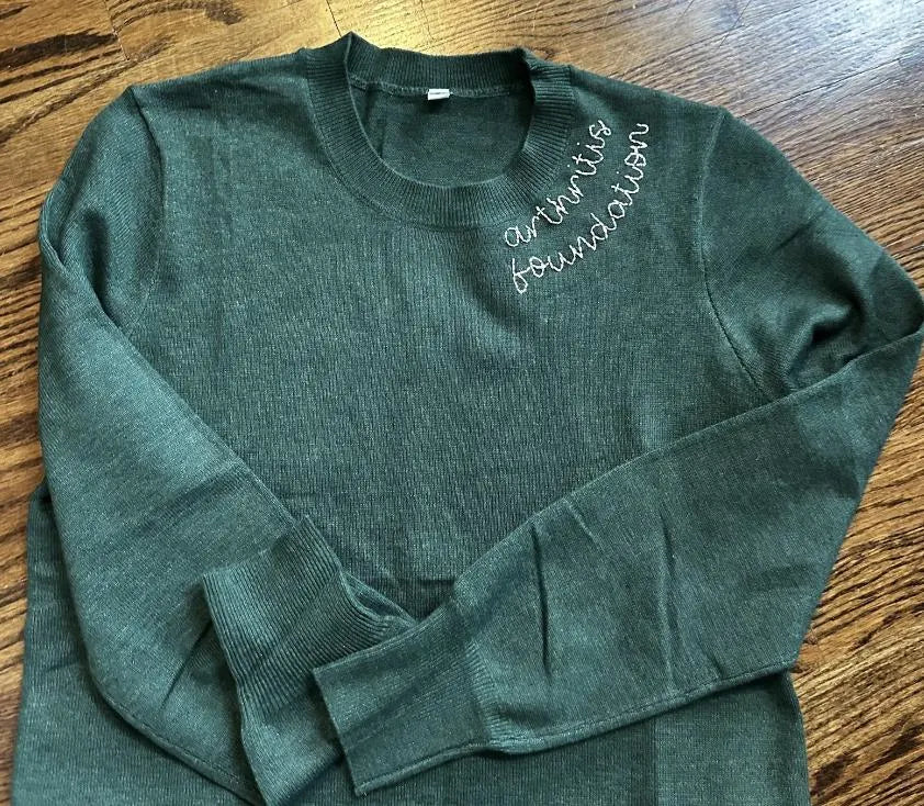 Green sweater with 'Arthritis Foundation' text on a wooden surface