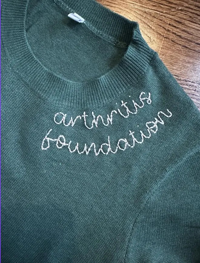 Green sweater with 'arthritis foundation' text on a wooden surface